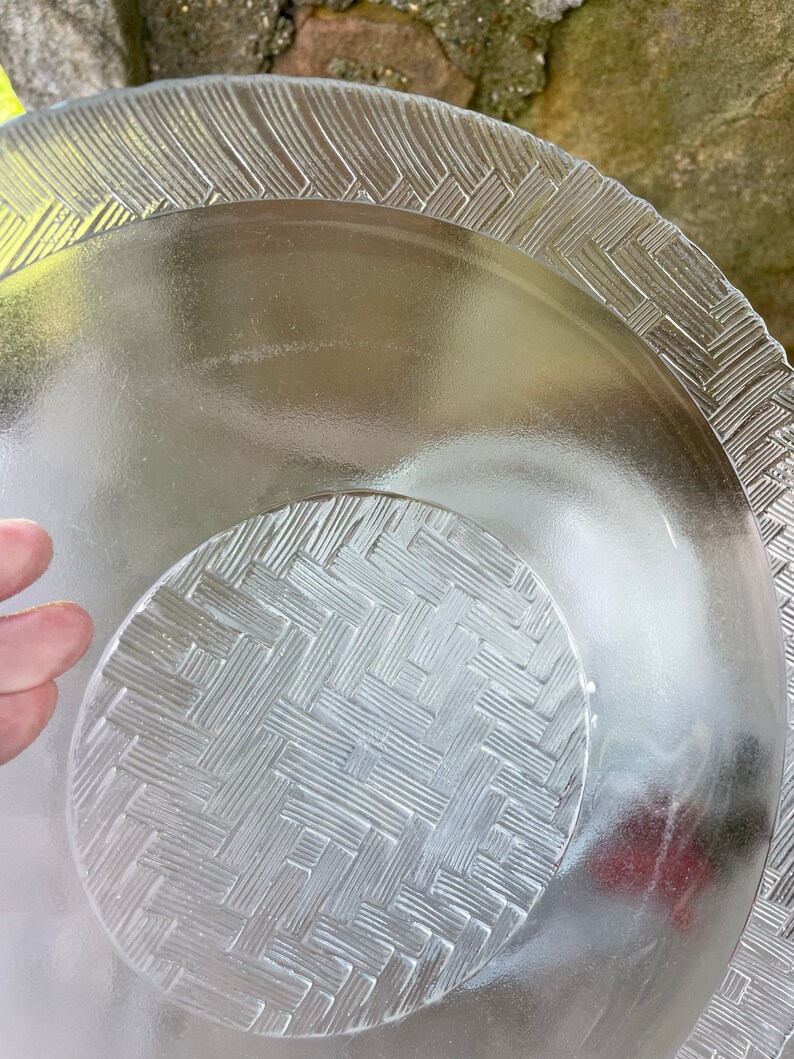 May include: Clear glass serving dishes with textured basketweave and geometric patterns. The set includes a large plate and a smaller, nested dish. The edges of the plates have a decorative, raised design.