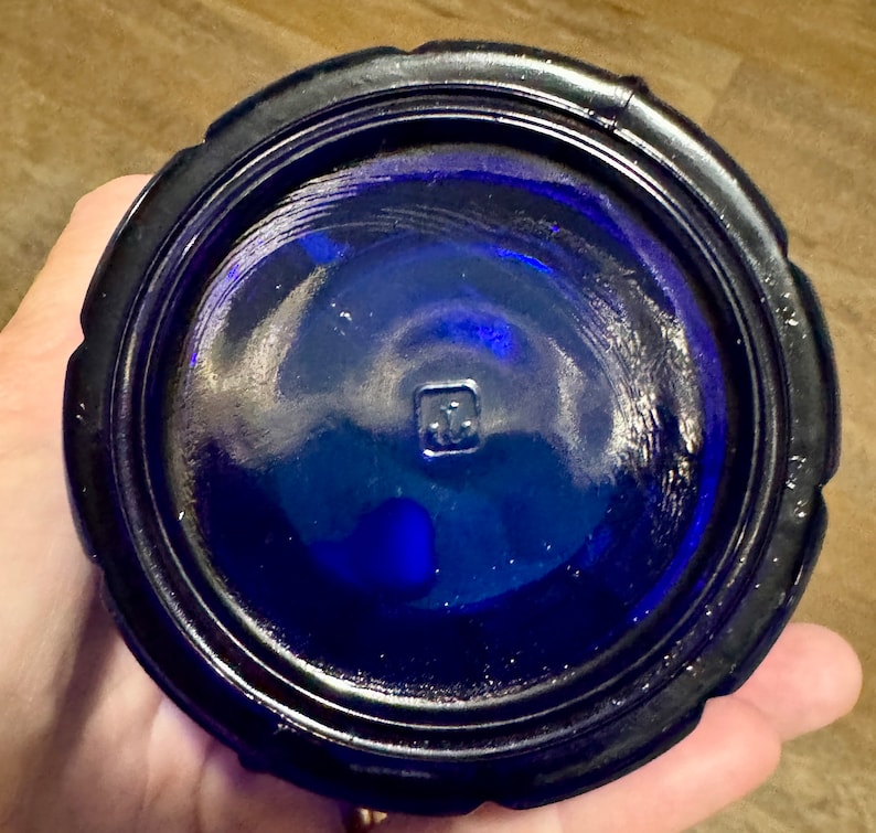 May include: Cobalt blue glass bottle with a textured rim and a square mark on the bottom.