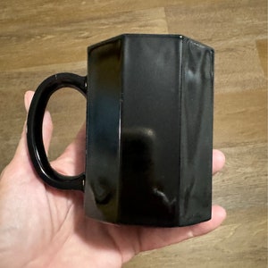 May include: A black ceramic mug with a hexagonal shape and a rounded handle.