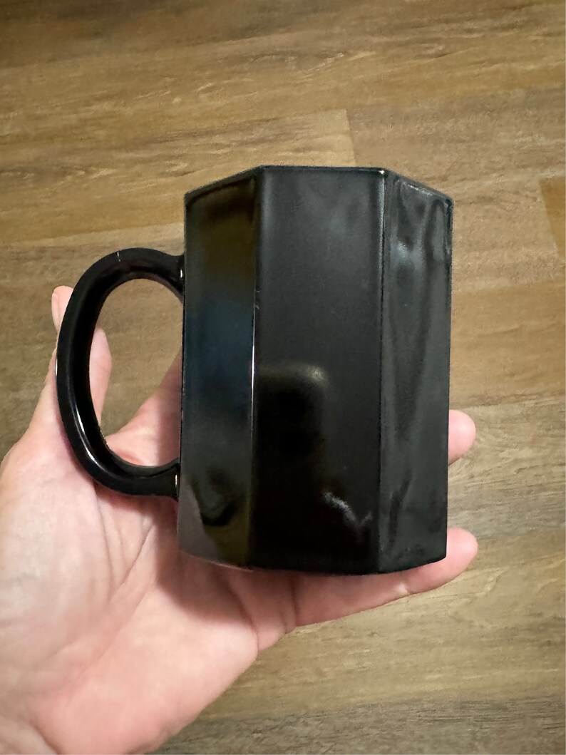 May include: A black ceramic mug with a hexagonal shape and a rounded handle.