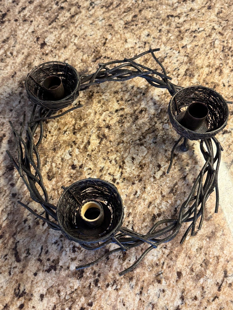 May include: A black metal wreath with three twig nests for candles. The wreath is made of twisted branches and has a rustic look.