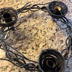 May include: A black metal candle holder shaped like a wreath with three candle holders. The candle holders are made of wire and have a rustic look.