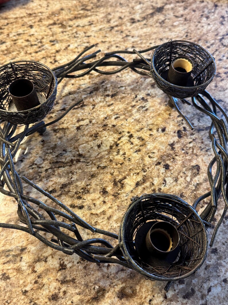 May include: A black metal candle holder shaped like a wreath with three candle holders. The candle holders are made of wire and have a rustic look.