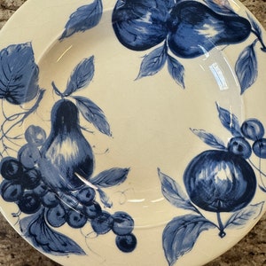 May include: A white ceramic plate with a blue and white fruit design. The plate features pears, grapes, and apples.