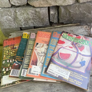 May include: A stack of six vintage The Workbasket magazines featuring various craft projects, including a crocheted watermelon, a crocheted cat, and a crocheted afghan. The magazines are from the 1970s and 1980s.
