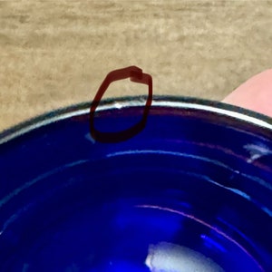 May include: A close-up of the rim of a cobalt blue ceramic bowl. The bowl has a white rim and a slight chip on the edge.