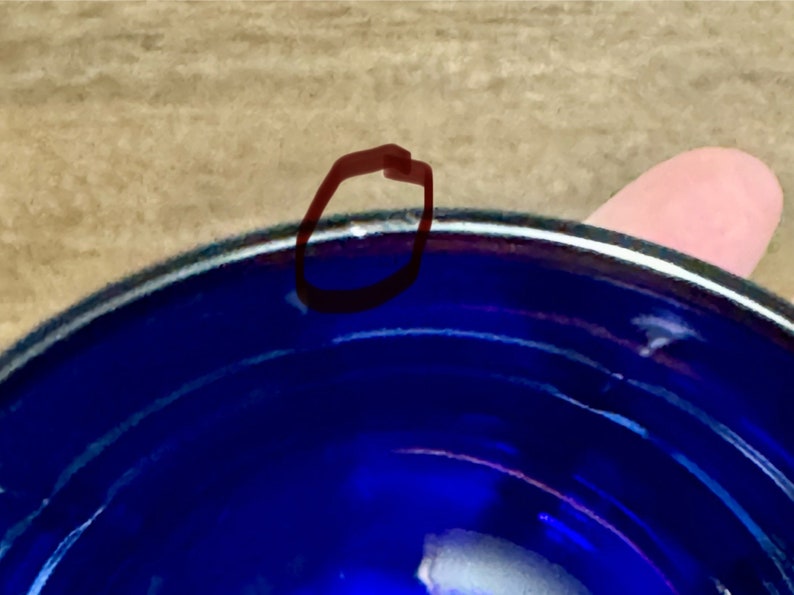 May include: A close-up of the rim of a cobalt blue ceramic bowl. The bowl has a white rim and a slight chip on the edge.