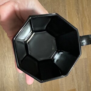 May include: A black octagonal ceramic mug with a handle. The mug has a smooth, glossy finish.