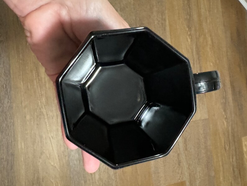 May include: A black octagonal ceramic mug with a handle. The mug has a smooth, glossy finish.