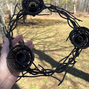 May include: A black metal wreath with four candle holders shaped like bird nests. The wreath is made of twisted metal branches.