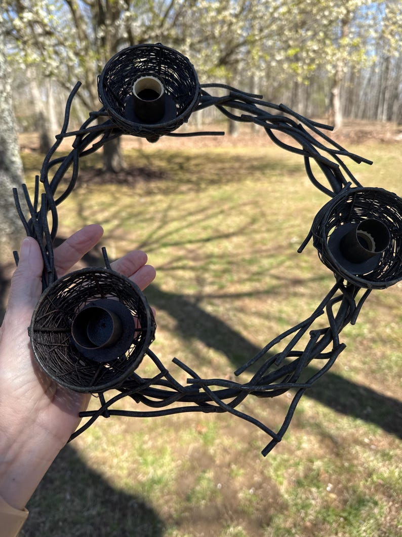 May include: A black metal wreath with four candle holders shaped like bird nests. The wreath is made of twisted metal branches.