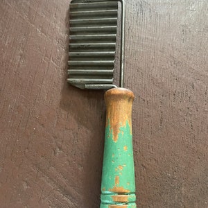 May include: A vintage metal and wood potato masher with a green painted handle. The masher has a series of ridges on the metal part to help crush potatoes.
