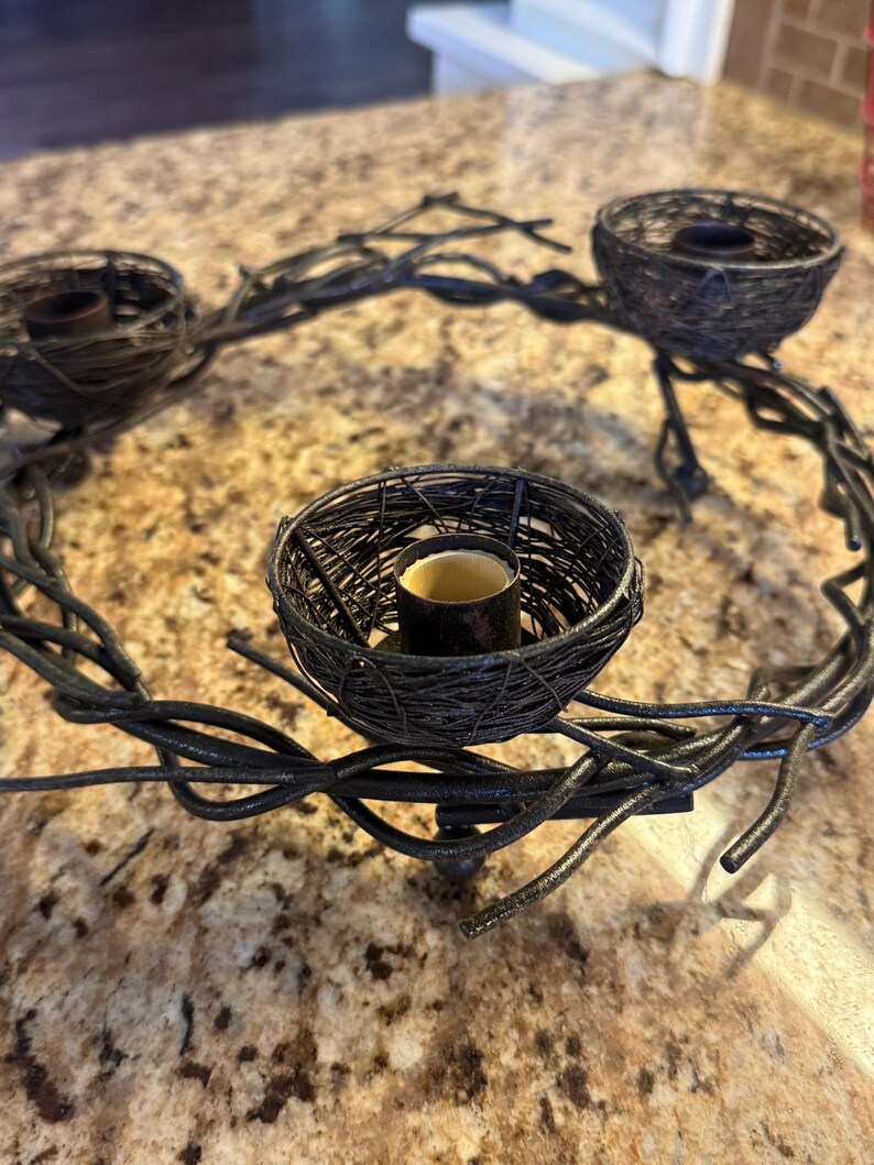 May include: A black metal candle holder shaped like a wreath with three bird's nest candle holders. The candle holder is made of twisted metal branches.