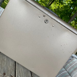 May include: A silver metal lock box with a keyhole and a handle. The box is sitting on a wooden surface.