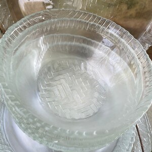 May include: Clear glass serving dishes with a woven basket pattern. The dishes include a stack of bowls and plates. The edges of the plates and bowls have a textured, ridged design. The dishes are stacked on top of each other.