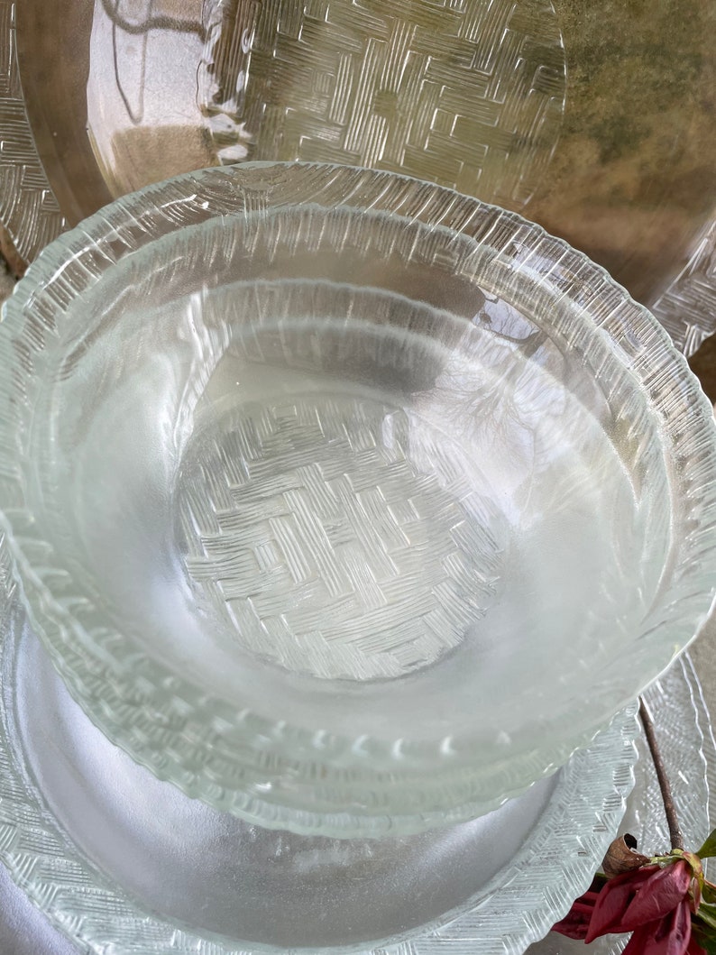 May include: Clear glass serving dishes with a woven basket pattern. The dishes include a stack of bowls and plates. The edges of the plates and bowls have a textured, ridged design. The dishes are stacked on top of each other.