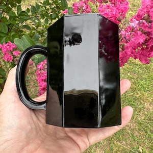 May include: A black octagonal mug with a handle. The mug is made of glass and has a glossy finish.