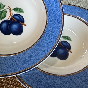 Pode incluir: Duas tigelas de sopa de cerâmica azul e branca com uma borda dourada e um design de ameixa. As tigelas estão empilhadas uma em cima da outra.