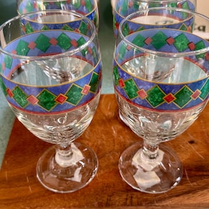 May include: Set of four clear wine glasses with a decorative band featuring blue, green, and red geometric patterns. The glasses have a classic stem and foot design, suitable for serving wine.