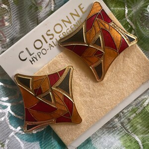 May include: A pair of gold-tone earrings with a geometric design. The earrings are made of red, orange, and black enamel. The earrings are labeled "CLOISONNE HYPO-ALLERGENIC".