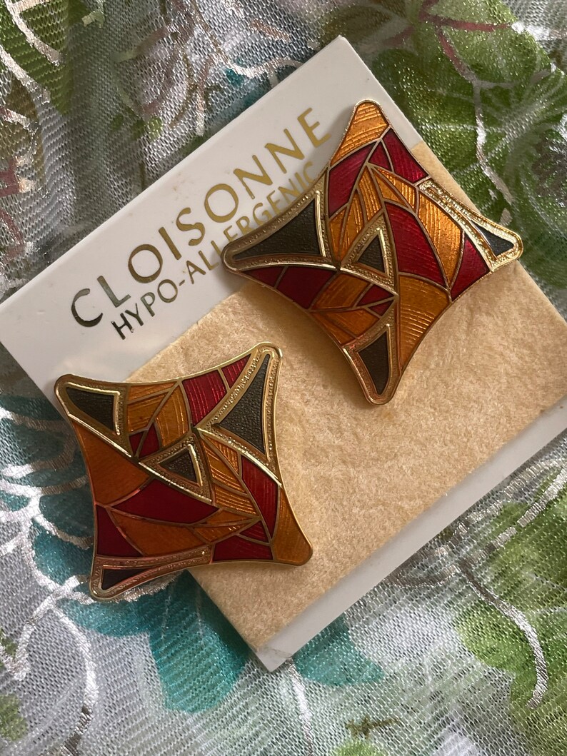 May include: A pair of gold-tone earrings with a geometric design. The earrings are made of red, orange, and black enamel. The earrings are labeled "CLOISONNE HYPO-ALLERGENIC".
