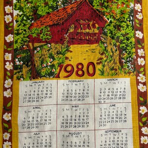 May include: A vintage yellow tea towel with a calendar for the year 1980. The calendar features a red barn with a yellow path leading to it. The barn is surrounded by green trees and white flowers.
