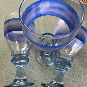 K&ouml;nnte beinhalten: Drei klare Weingl&auml;ser aus Glas mit blau-wei&szlig;en Streifenmustern. Die Gl&auml;ser haben eine abgerundete Schale und einen hohen, schlanken Stiel.