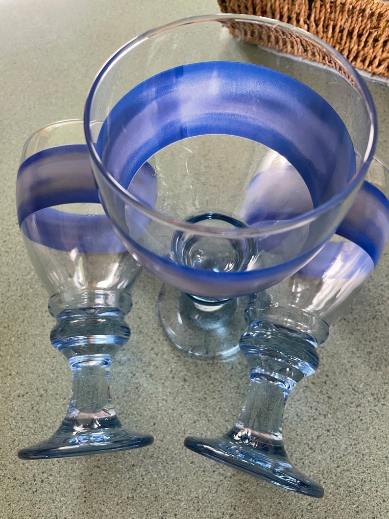 K&ouml;nnte beinhalten: Drei klare Weingl&auml;ser aus Glas mit blau-wei&szlig;en Streifenmustern. Die Gl&auml;ser haben eine abgerundete Schale und einen hohen, schlanken Stiel.