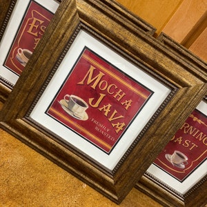 May include: Three framed prints with a coffee theme. The center print features a red background with the text "Mocha Java" and "Freshly Roasted". The print on the left features a brown background with the text "Espresso". The print on the right features a red background with the text "Morning Roast".