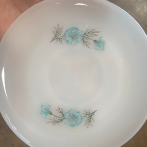 Puede incluir: Plato de cer&aacute;mica blanco con un dise&ntilde;o floral azul. Las flores son estilizadas y tienen un color azul claro con tallos y hojas verdes.
