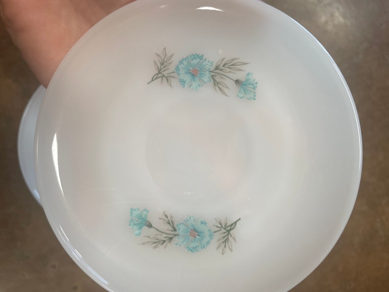 Puede incluir: Plato de cer&aacute;mica blanco con un dise&ntilde;o floral azul. Las flores son estilizadas y tienen un color azul claro con tallos y hojas verdes.