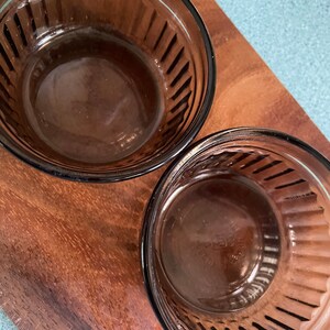 May include: Two brown glass ramekins with fluted edges. The ramekins are empty and sitting on a wooden surface.