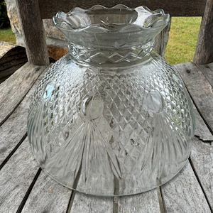 Könnte beinhalten: Ein klarer Glasschirm mit Rautenmuster und gewelltem Rand. Der Vintage-Lampenschirm steht auf einer verwitterten Holzoberfläche. Der Schirm hat eine große, abgerundete Schalenform.