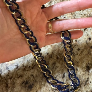 May include: A gold chain necklace with blue enamel accents. The chain is made of interlocking links.