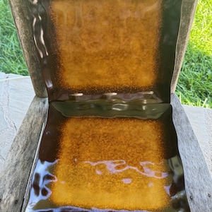 Puede incluir: Dos platos cuadrados de cerámica con un diseño moteado marrón y dorado. Los platos tienen un borde marrón oscuro y un centro dorado texturizado y moteado. Los platos están sobre una superficie de madera.