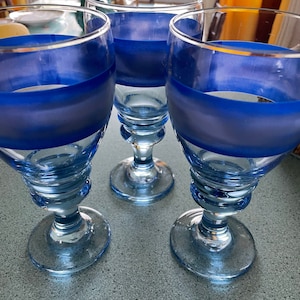 May include: Three blue and clear glass goblets with a blue stripe around the middle of each goblet.
