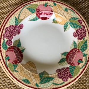 Pode incluir: Uma tigela de sopa de cerâmica branca com um design de mosaico que apresenta frutas e folhas em tons de vermelho, verde, amarelo e roxo.