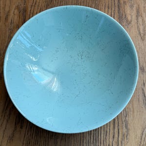 May include: A round, light blue bowl with a speckled pattern. The bowl has a smooth, glossy finish and a slightly curved rim. The bowl is likely made of ceramic or porcelain and is suitable for serving food.
