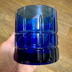 May include: A cobalt blue glass tumbler with a square patterned design. The tumbler is made of thick glass and has a rounded bottom.
