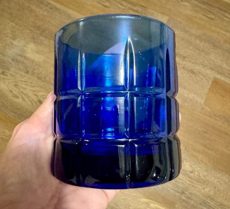 May include: A cobalt blue glass tumbler with a square patterned design. The tumbler is made of thick glass and has a rounded bottom.
