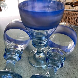 K&ouml;nnte beinhalten: Drei klare Glaskelche mit blauen, bemalten B&auml;ndern um den oberen und unteren Rand der Schale. Die Kelche haben einen dicken, klaren Glasstiel und einen breiten, klaren Glasfu&szlig;.