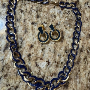 May include: A gold and blue chain necklace with matching earrings. The necklace is made of large, linked circles with a gold interior and a blue exterior. The earrings are hoop-shaped with a blue enamel center.