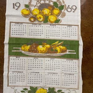 May include: A vintage 1969 calendar tea towel with a green and yellow fruit design. The calendar features a basket of fruit and a platter of fruit. The months of the year are listed with the days of the week.