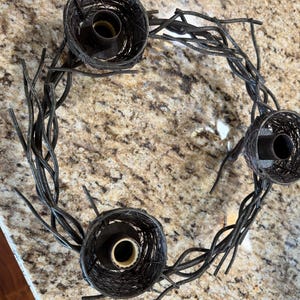 May include: A black metal candle holder shaped like a nest with three candle holders. The candle holder is made of twisted metal branches.