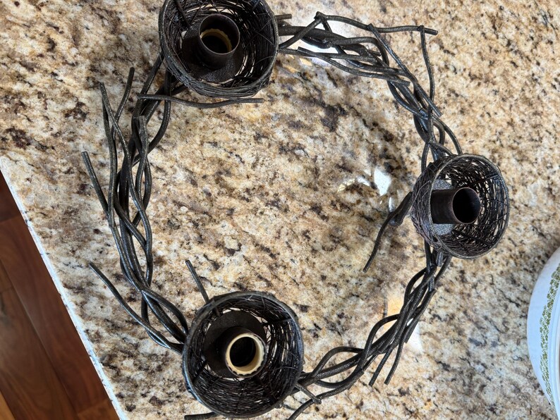May include: A black metal candle holder shaped like a nest with three candle holders. The candle holder is made of twisted metal branches.