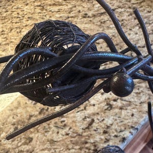 May include: A black metal sculpture with a circular design. The sculpture is made of twisted wire and has a rustic finish.