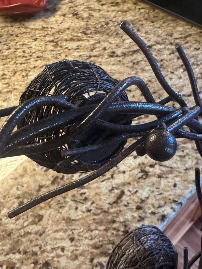 May include: A black metal sculpture with a circular design. The sculpture is made of twisted wire and has a rustic finish.