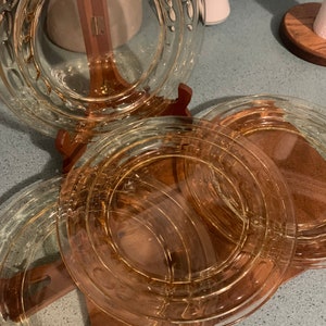 May include: Set of four clear glass dinner plates with a raised, textured rim. The plates are stacked on a wooden stand.