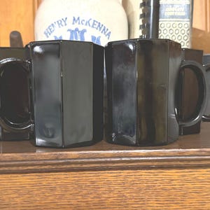 May include: Four black octagonal mugs with handles. The mugs are made of glass and have a shiny finish.