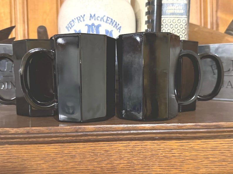 May include: Four black octagonal mugs with handles. The mugs are made of glass and have a shiny finish.